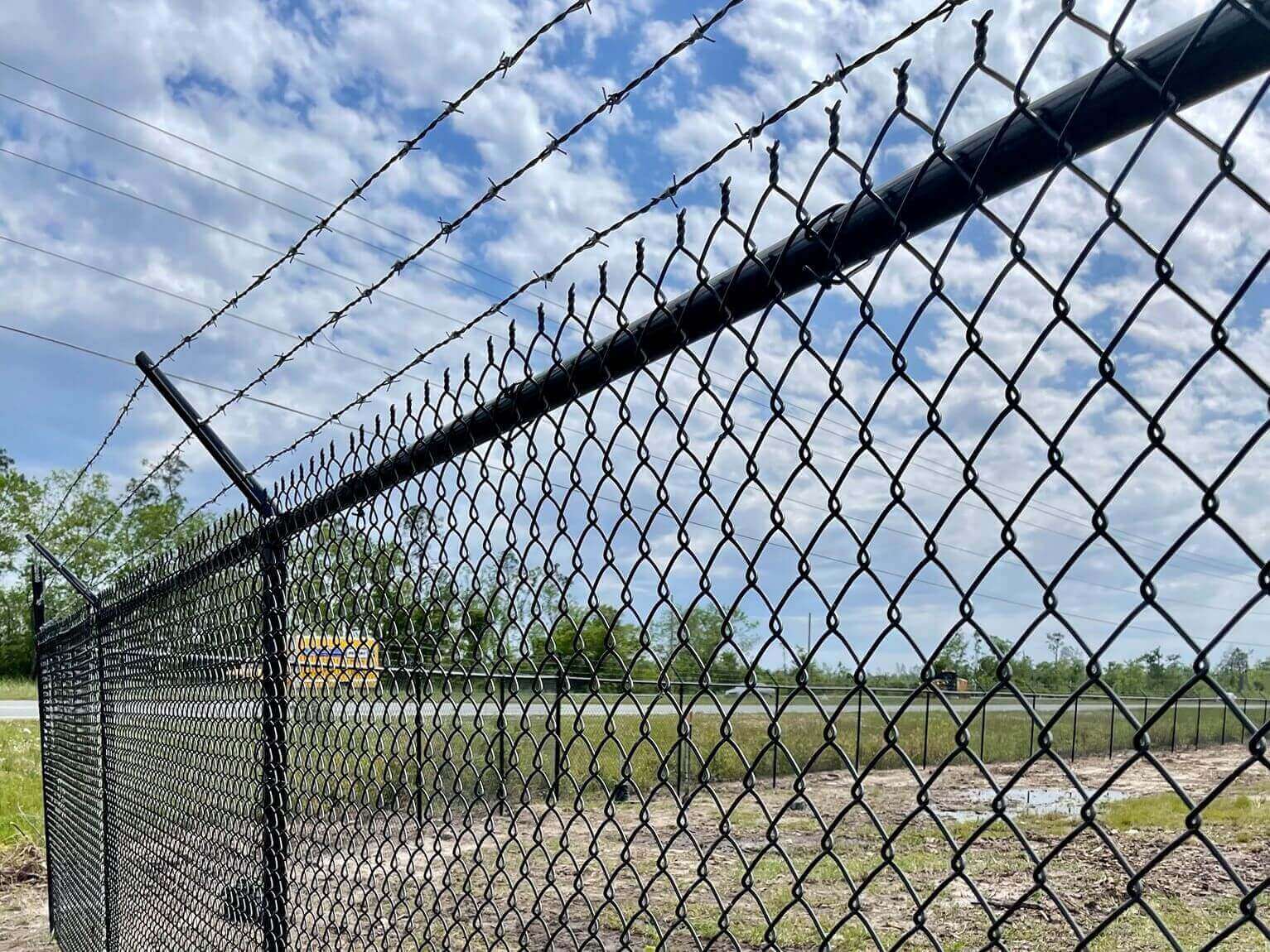 Photo of a black pvc coated chain link fence with barbed wire
